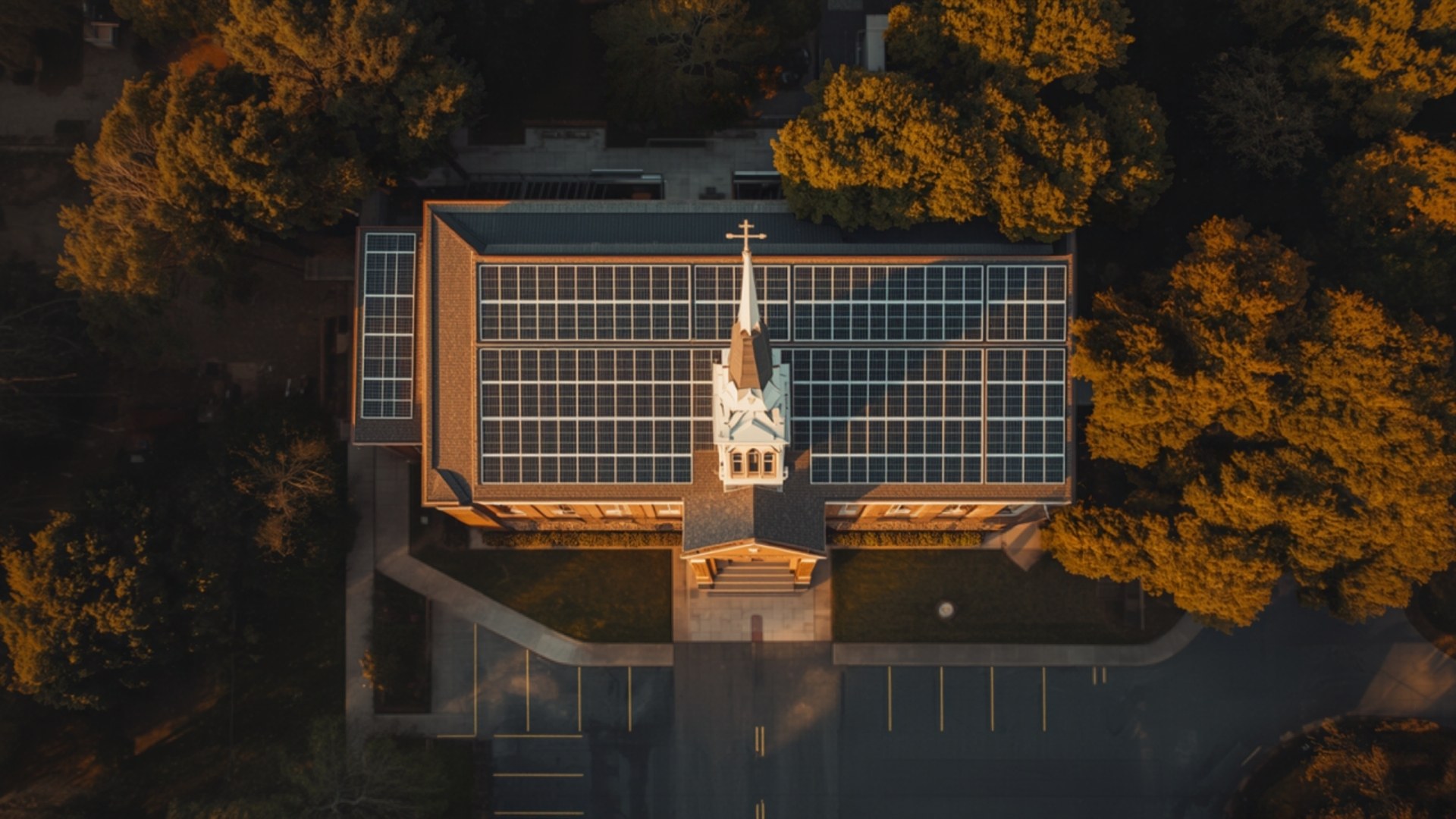 Aerial view at golden hour of a church with a clock tower and solar panels covering its roof